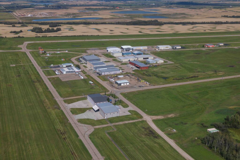 Vue aérienne d'un groupe de hangars et de routes d'accès à l'aéroport de Villeneuve, avec la piste et des terres agricoles au-delà