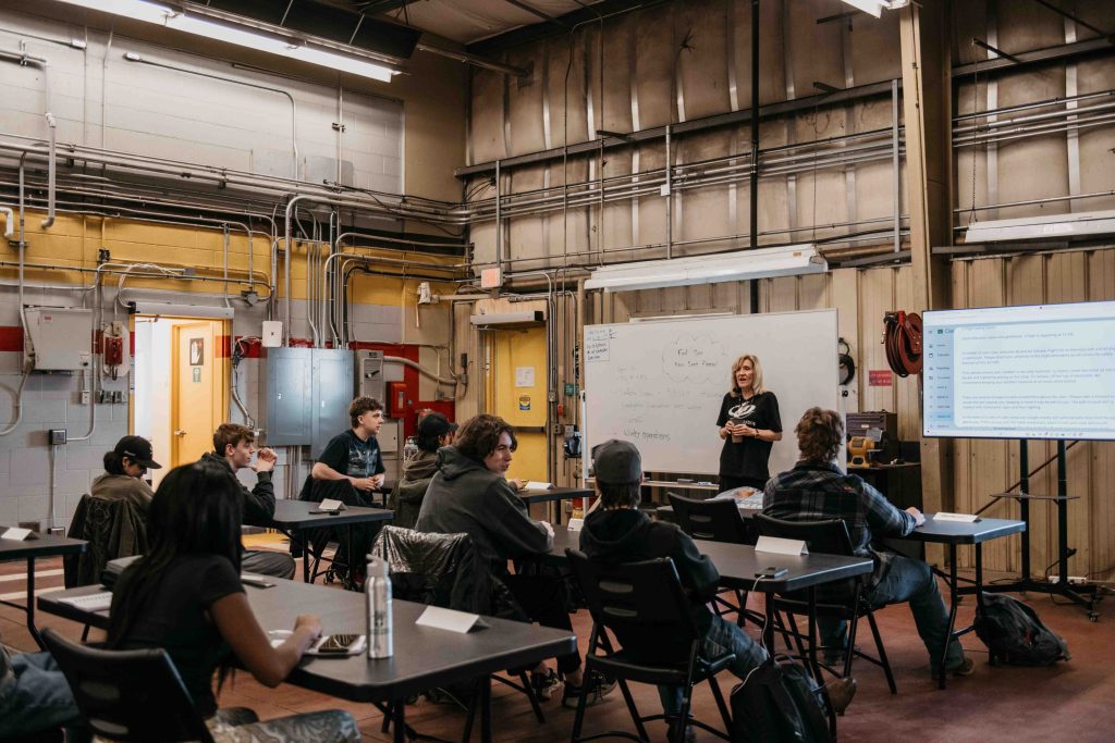 Instructrice enseignant à un groupe d’élèves dans une salle de formation de type hangar dans le cadre du Parcours aéronautique de ZVL à l’aéroport de Villeneuve